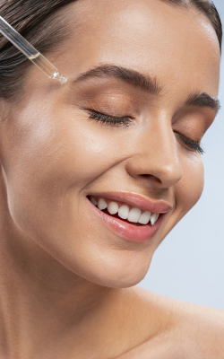 a close-up of a smiling woman with dropper on forehead