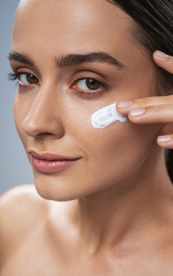 close up of women looking towards left and applying cream on cheek